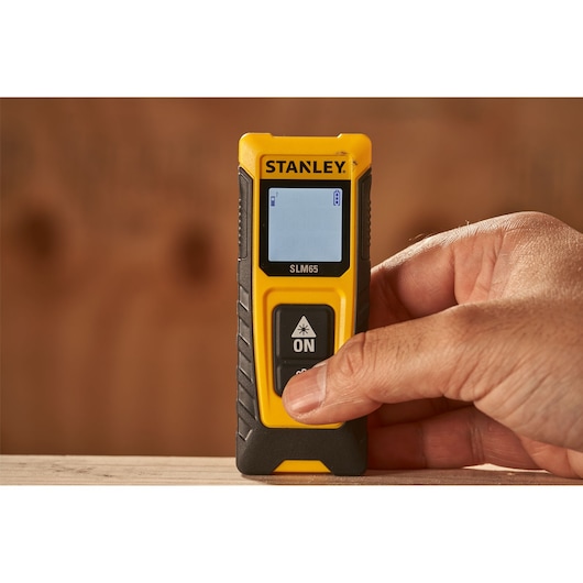 Photo du télémètre laser STANLEY STHT77065-0 jaune et noir tenu à la main, vue rapprochée.