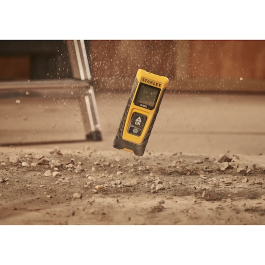 Télémètre laser STANLEY STHT77065-0 jaune et noir tombant sur un sol poussiéreux.
