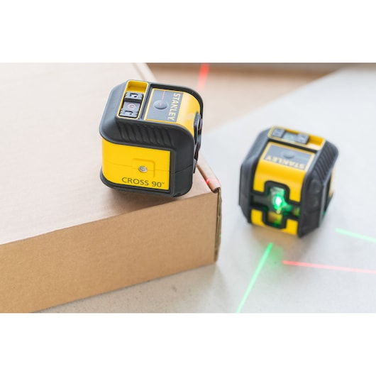STANLEY STHT77502-1 geel-zwarte kruislijnlaser, twee units op oppervlakken die groene en rode lijnen uitstralen.