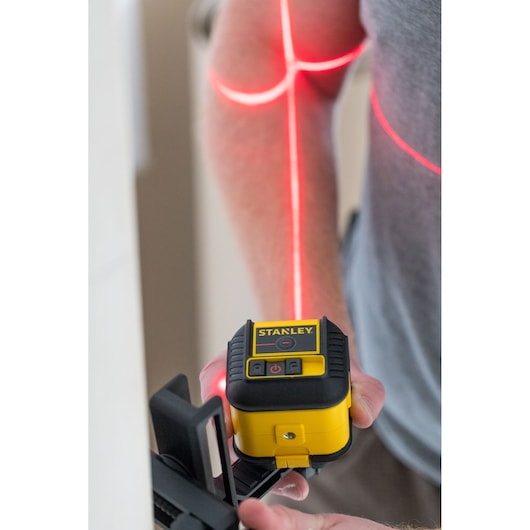 STANLEY STHT77502-1 geel-zwarte kruislijnlaser in gebruik met geprojecteerde rode laserlijnen.