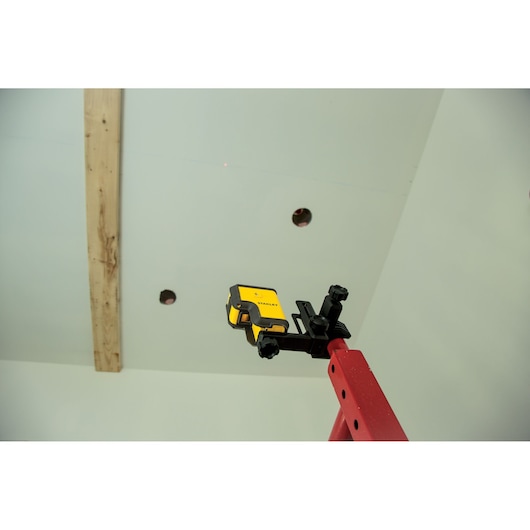 STANLEY STHT77503-1 laserwaterpas bevestigd aan rode ladder bij plafondinstallatie.