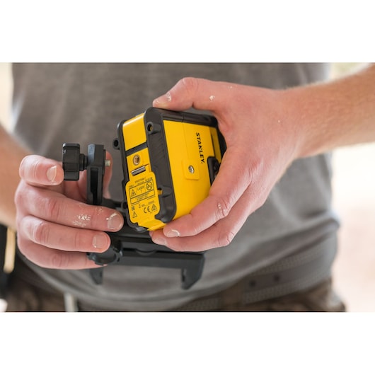 Photo du niveau laser jaune et noir STANLEY STHT77504-1 tenu dans les mains, contexte de chantier.
