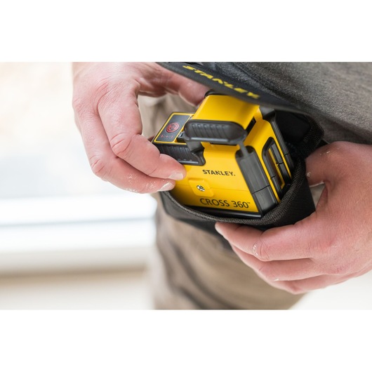 STANLEY STHT77504-1 gele CROSS 360° laserwaterpas wordt met de hand in een zwart draagetui geplaatst.