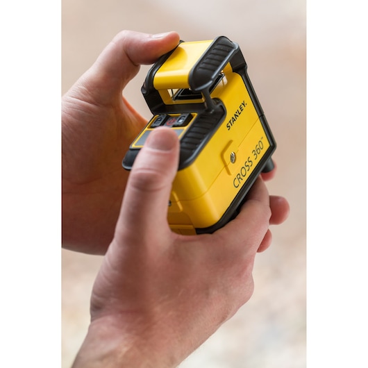 Photo du niveau laser STANLEY STHT77504-1 CROSS 360 tenu dans les mains, extérieur jaune et noir.