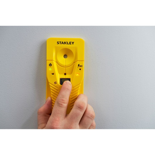 STANLEY STHT77587-0 gele balkzoeker tegen de muur, persoon drukt op knop, vooraanzicht.