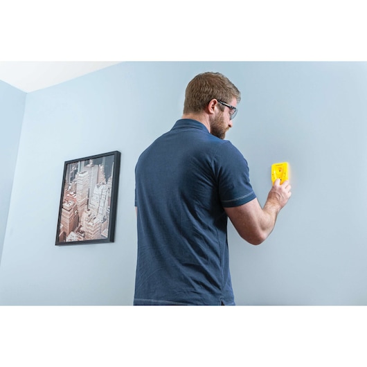 STANLEY STHT77587 balkendetector tegen blauwe muur thuis, persoon gebruikt het apparaat.