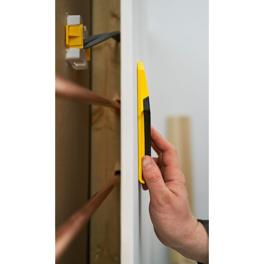 STANLEY STHT77588-0 gele balkzoeker tegen muur gehouden, zijaanzicht, elektrische draden op achtergrond