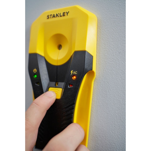 Foto van STANLEY STHT77588-0 digitale balkzoeker, geel-zwart, indicatorlampjes zichtbaar, tegen een muur.