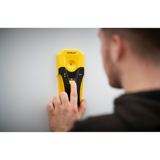 STANLEY STHT77588-0 balkzoeker tegen een muur in gebruik, foto met hand die op knop drukt.