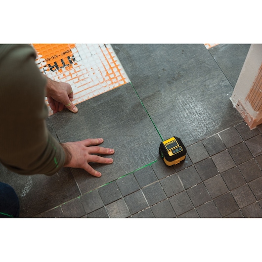 STANLEY STHT77592-1 laserwaterpas gebruikt voor tegeluitlijning op een grijze vloer tijdens installatie.