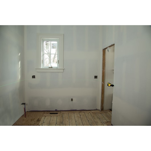 STANLEY STHT77594-1 laserwaterpas projecteert een groene lijn in een onafgewerkte kamer, gemonteerd aan de rechterwand.