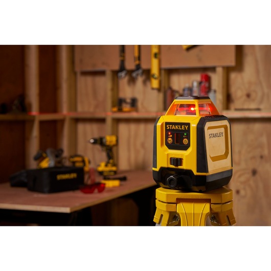 Niveau laser STANLEY STHT77616-0 sur trépied dans un atelier avec outils et établi en arrière-plan.