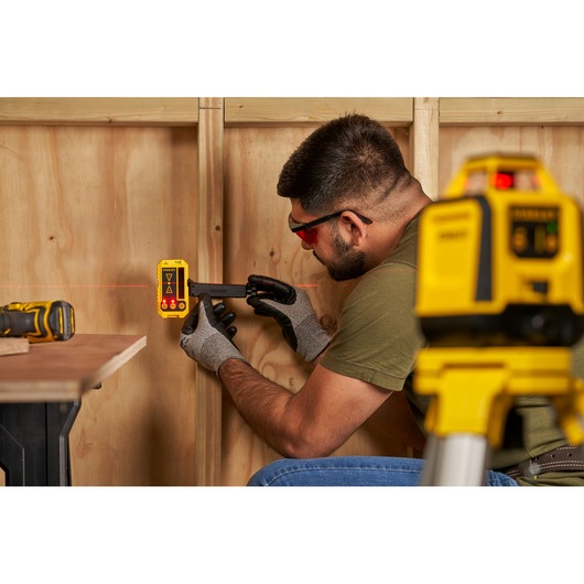 STANLEY STHT77616-0 détecteur laser utilisé pour l'alignement des murs, avec gants et équipement laser.