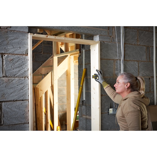 STANLEY STHT77666-0 télémètre laser utilisé par une personne sur un cadre de porte en bois sur un chantier.