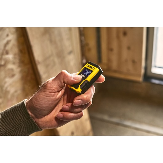 Télémètre laser compact STANLEY STHT77666-0 jaune et noir tenu en main, intérieur.