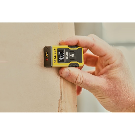 STANLEY STHT77666-0 télémètre laser tenu contre un mur, écran numérique visible.