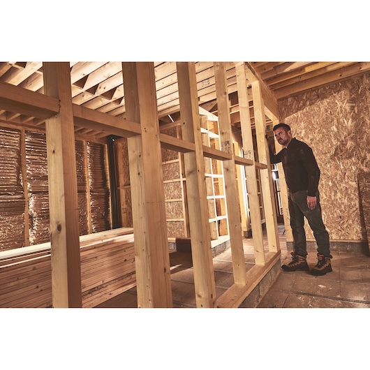 STANLEY STHT77666-0 photographie d’un ouvrier inspectant une charpente en bois sur chantier non terminé.