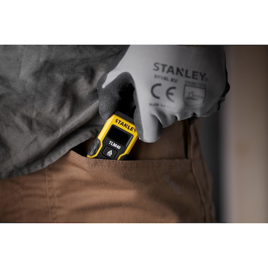 Télémètre laser STANLEY STHT77666-0 rangé dans une poche par une main gantée.