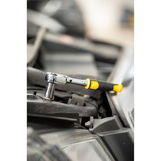 STANLEY STMT82663-0 ratelsleutel met geel-zwart handvat gebruikt op auto-onderdeel, zijaanzicht.
