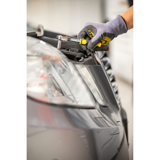 STANLEY STMT82663-0 ratelsleutel gebruikt op autokoplamp, close-up met gehandschoende hand.