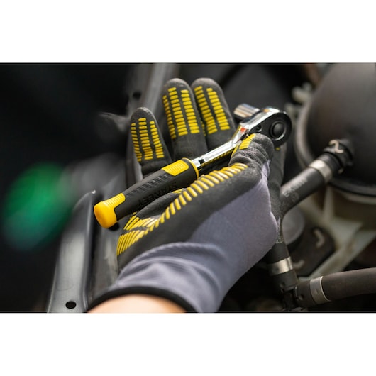 STANLEY STMT82663-0 ratelgereedschap met zwart-gele handgreep, vastgehouden door een handschoen tijdens auto werkzaamheden.