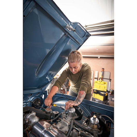 Foto van STANLEY STMT82665-0 1272-ToothRatchet gebruikt op een motor, gebruiker draait bout aan, werkplaats op de achtergrond.