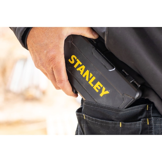 Foto van een hand die een zwarte STANLEY STMT82672-0 gereedschapskoffer in een gereedschapsriemzak steekt, close-up.
