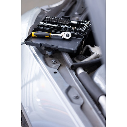 STANLEY STMT82672-0 dopsleutel- en ratelset met gele handgreep, open koffer op een motorruimte, schuine hoek.