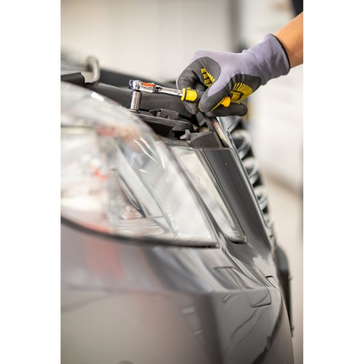 STANLEY STMT82828-1 ratelschroevendraaier draait bout aan autokoplamp vast, close-up.