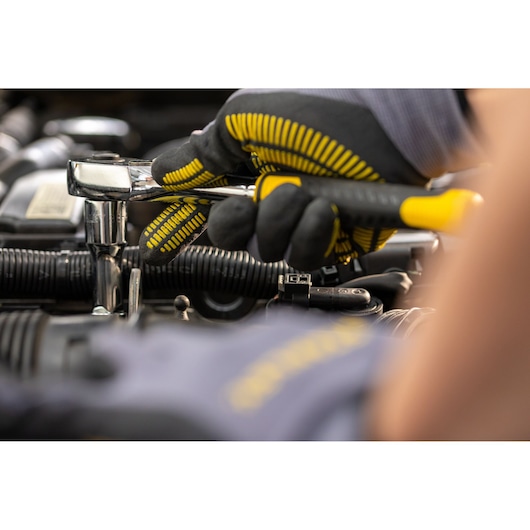 STANLEY STMT82830-1 ratelsleutel gebruikt met handschoenen bij automotor, close-up foto.