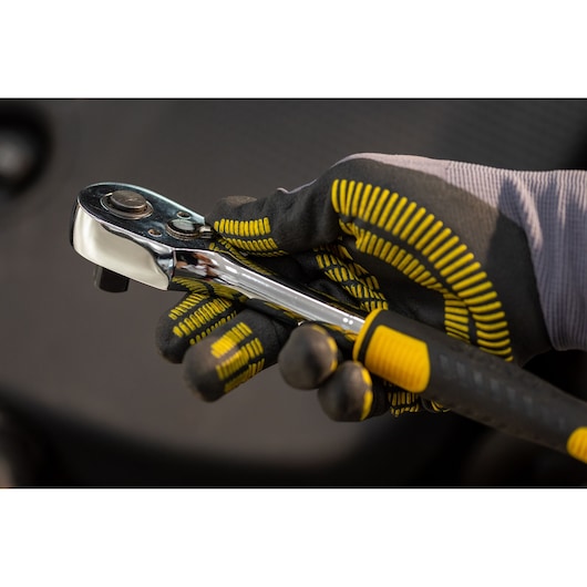 STANLEY STMT82830-1 ratelsleutel vastgehouden in gehandschoende hand, chroomafwerking met zwart-gele greep.