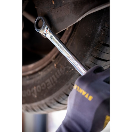 Photo de la clé mixte STANLEY STMT82842-0 utilisée sur un boulon de pneu de voiture, tenue par une main gantée.