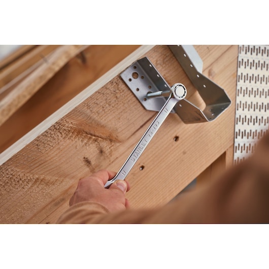 Photo de la clé mixte STANLEY STMT82843-0 utilisée pour serrer un boulon sur une équerre métallique et un cadre en bois.