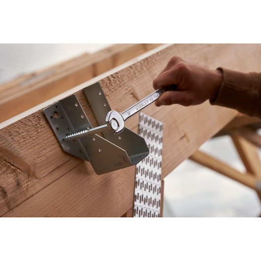 Clé mixte STANLEY STMT82843-0 serrant un boulon sur une poutre en bois, gros plan sur un chantier.
