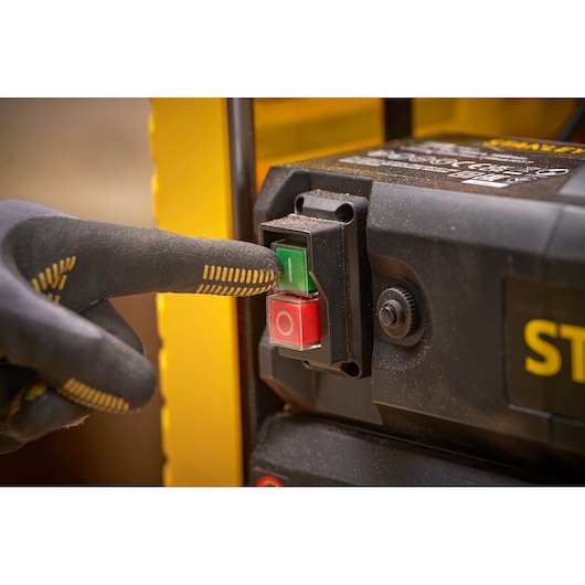 STANLEY STP18-B2 interrupteur d’alimentation de machine avec une main gantée appuyant sur le bouton vert, vue rapprochée.