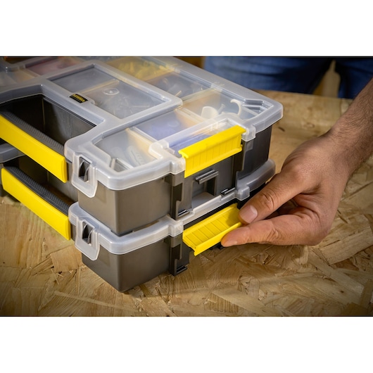 STANLEY STST1-70720 boîte organisatrice avec loquet jaune, empilée, gros plan sur une main ouvrant le loquet.