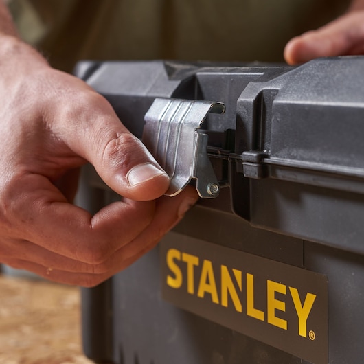 Boîte à outils STANLEY STST1-75518-KR gros plan, main ouvrant la fermeture métallique, boîtier noir, logo jaune.