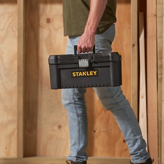 Photo de boîte à outils noire STANLEY STST1-75518-KR portée par une personne en jeans, fond en bois.