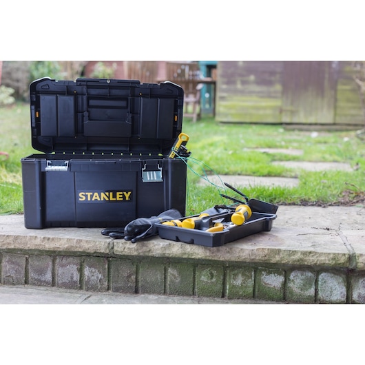 STANLEY STST1-75521 zwarte gereedschapskist open met geel handgereedschap en handschoenen op een stenen trede.