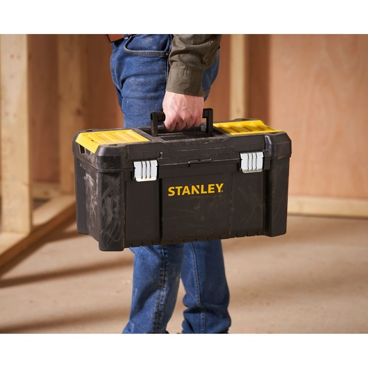 Stanley STST1-75521 zwarte en gele gereedschapskist gedragen door persoon, in een werkplaats.