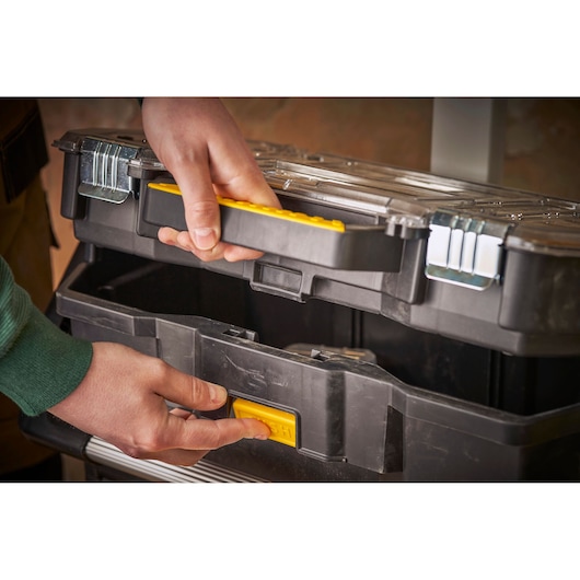 STANLEY STST1-79231 zwarte gereedschapskoffer met gele handgreep en sluiting, handen openen in close-up.
