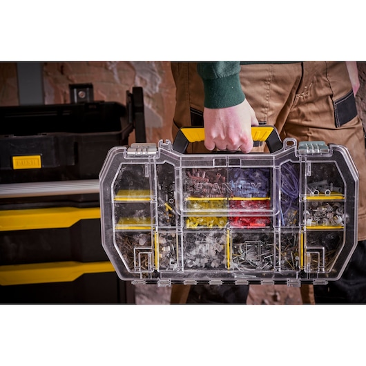 STANLEY STST1-79231 organizer met gele handgreep, doorzichtige deksel en hardwarevakken, in de hand gedragen.