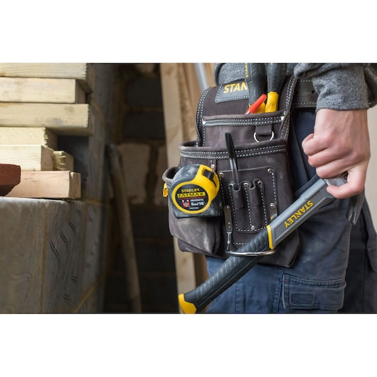 STANLEY STST1-80114 gereedschapsriem met rolmaat, handgereedschap en hamer op een bouwplaats.