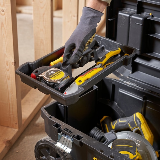 Gros plan sur la boîte à outils STANLEY STST1-80150 avec une main soulevant le plateau contenant un mètre, un couteau et une pince.
