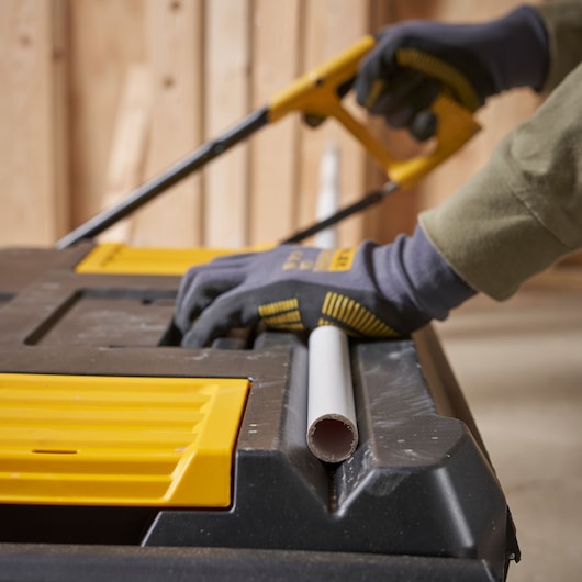 Boîte à outils STANLEY STST1-80150 utilisée comme surface de travail, personne avec gants sciant un tuyau, photographie en gros plan.