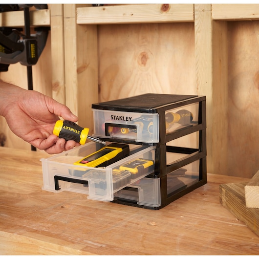 STANLEY STST40710-1 organiseur à tiroirs avec trois tiroirs transparents, posé sur un établi, contenant des outils à main.