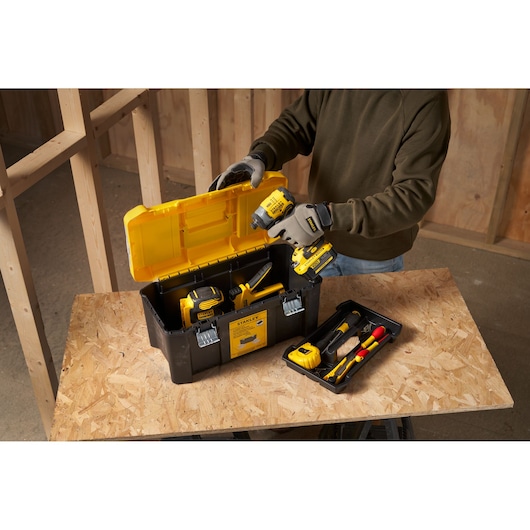 STANLEY STST75787-1 boîte à outils avec couvercle jaune, remplie d’outils électriques et accessoires sur établi.