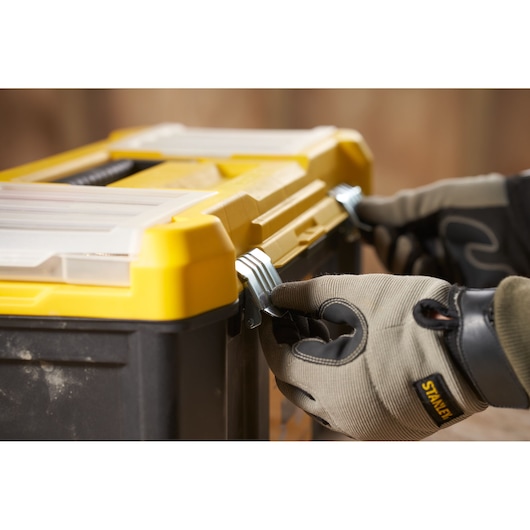 STANLEY STST75787-1 boîte à outils en gros plan avec mains gantées fermant les loquets métalliques, produit photo.
