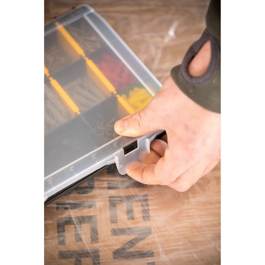STANLEY STST81680-1 organiseur de petites pièces avec couvercle transparent, séparateurs jaunes, main ouvrant le loquet, vue en angle.