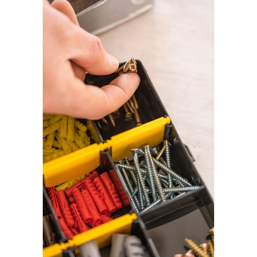 Organiseur STANLEY STST81681-1 avec main prenant des vis, chevilles murales et fixations assorties visibles.